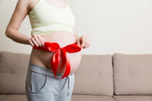 Ventre d'une femme enceinte attachée avec un arc rouge sur un fond d'accueil