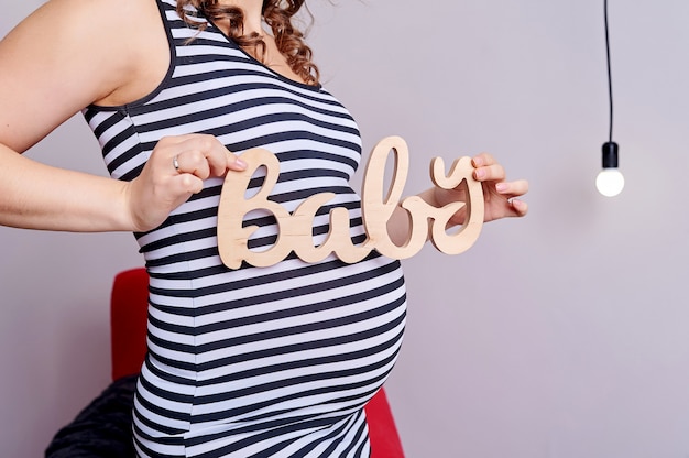 Ventre de femme enceinte avec symbole texte bébé dans ses mains