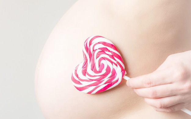 Photo ventre de jeune femme enceinte avec des bonbons coeur sur un bâton