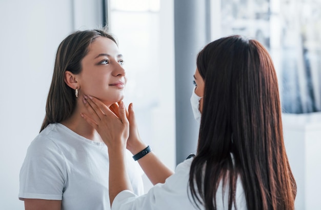 Vérification des ganglions lymphatiques et de la gorge Une jeune femme rend visite à une femme médecin dans une clinique moderne