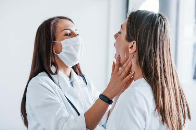 Vérification des ganglions lymphatiques et de la gorge Une jeune femme rend visite à une femme médecin dans une clinique moderne