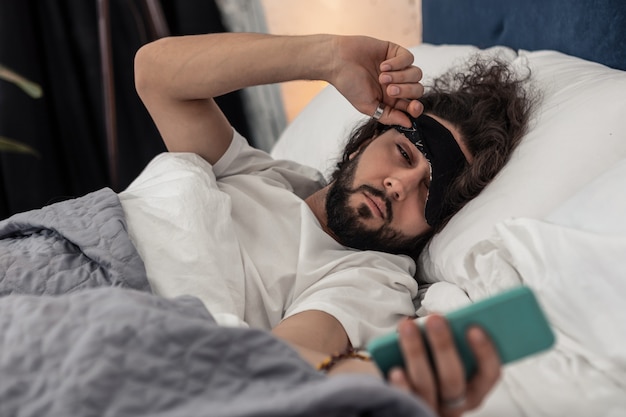 Vérification de l'heure. Bel homme endormi regardant son téléphone tout en vérifiant l'heure le matin