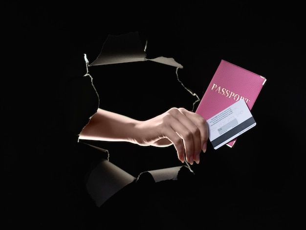Vérification de l'identité de fraude bancaire Sécurité des données personnelles Main féminine montrant une carte de crédit passeport avec numéro CVV à l'intérieur d'un trou de papier percé noir mur déchiré isolé sur noir