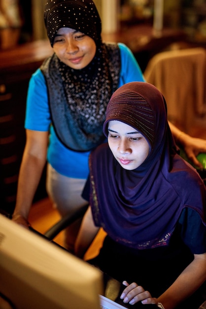 Vérification des réservations en ligne à la réception de l'hôtel Photo de deux femmes thaïlandaises musulmanes travaillant sur un ordinateur à la réception d'un hôtel