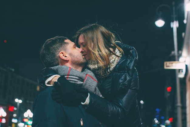 Véritable jeune couple marchant ensemble dans la ville de nuit, s&#39;embrasser