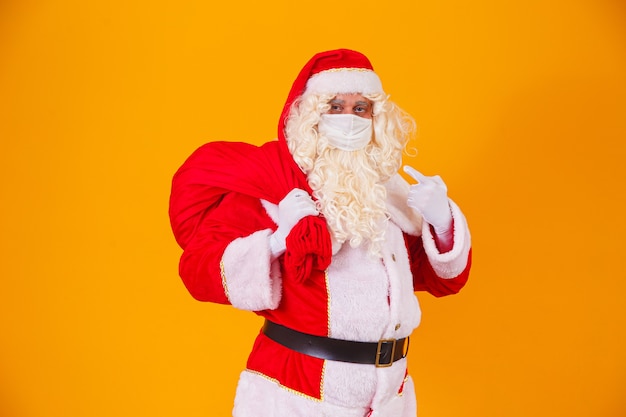Véritable Père Noël sur fond jaune, portant un masque de protection contre le covid19. Noël avec distance sociale. Covid-19