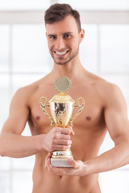 Photo véritable réussite. beau jeune homme musclé tenant un trophée d'or dans ses mains et souriant