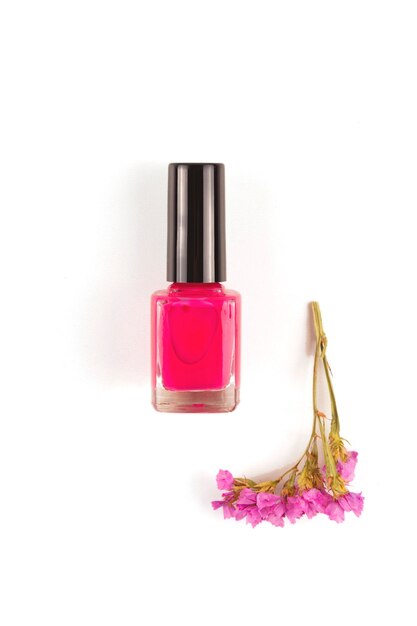 Vernis à ongles fuchsia brillant sur une surface blanche à côté d'une fleur de la même couleur