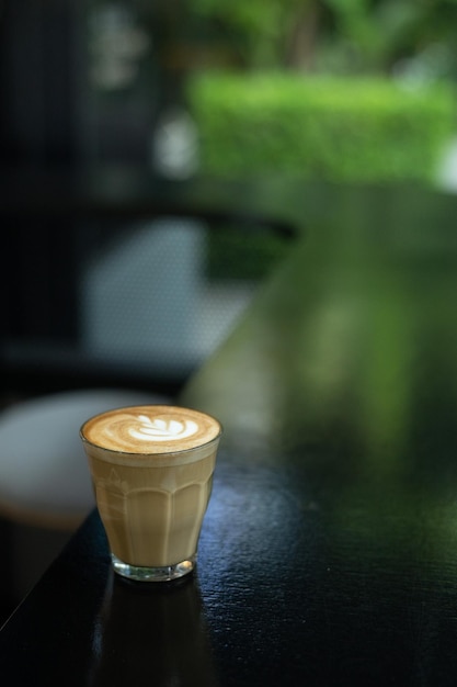 Un verre d'art latte est posé sur une table avec une table noire devant une fenêtre.