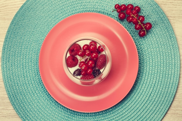 Un verre avec des baies et du yaourt sur une assiette rose en vue de dessus