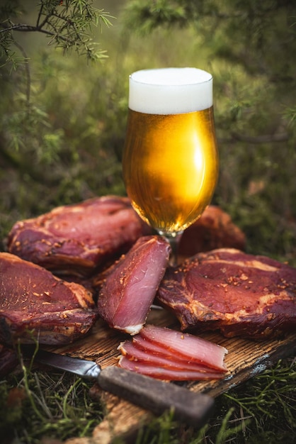 Verre de bière artisanale glacée avec de la viande de porc fumée à froid maison sur une planche de bois rustique