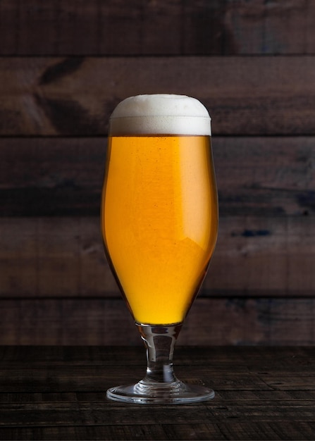 Verre de bière blonde dorée avec mousse sur bois