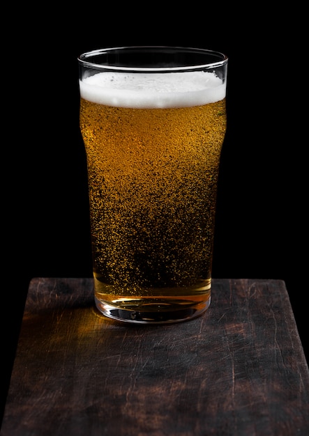 Verre de bière blonde avec mousse et bulles à bord de pierre sur fond noir.