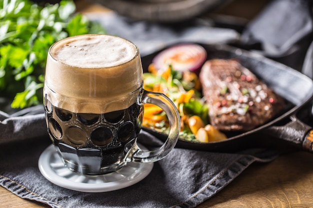 Verre de bière brune au pub ou au restaurant sur table avec de la nourriture délicieuse.