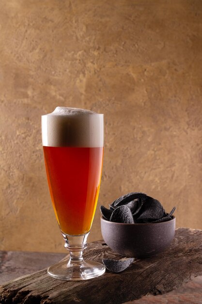 Un verre de bière avec de la mousse et une tasse avec des copeaux noirs se dresse sur une planche de bois