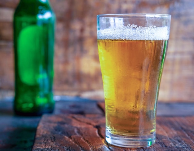 Verre à bière pétillante et bouteille de bière verte sur table en bois