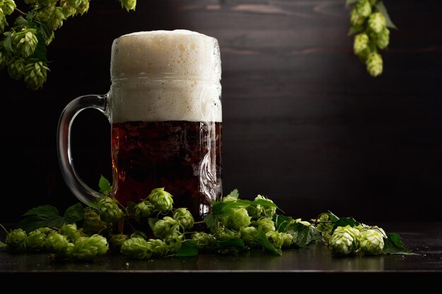 Verre à bière plein sur fond de bois avec du houblon