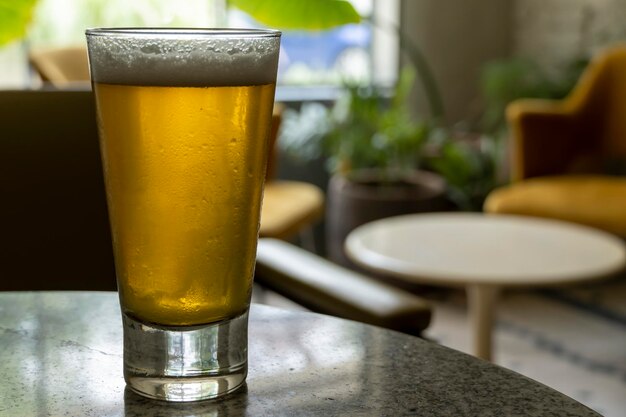 Verre de bière sur une table en terrazzo deux chaises jaunes en arrière-plan fenêtre de table rétro avec lumière naturelle