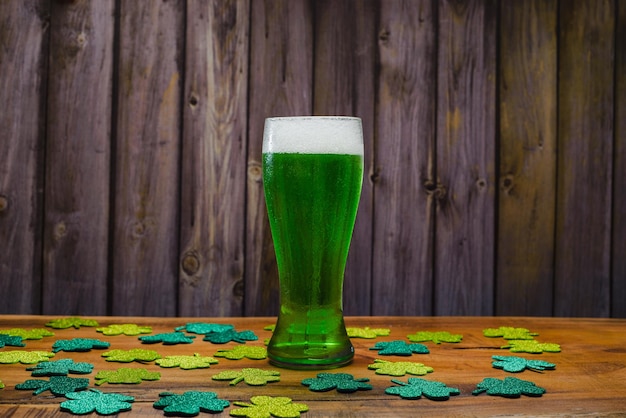 Verre de bière verte sur une table en bois avec des trèfles scintillants