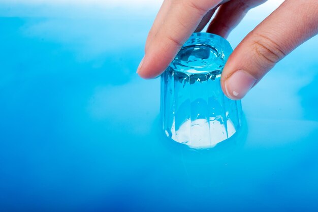 Un verre bleu dans la main sur de l'eau bleue