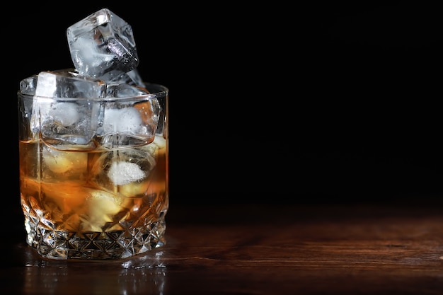 Un verre de boisson alcoolisée forte avec de la glace sur un comptoir de bar en bois. Whisky avec des glaçons. Verre avec une boisson fraîche.