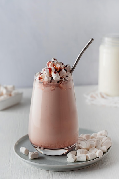 Un verre de boisson au cacao décoré de guimauve et de sirop servi sur assiette avec une collation sucrée