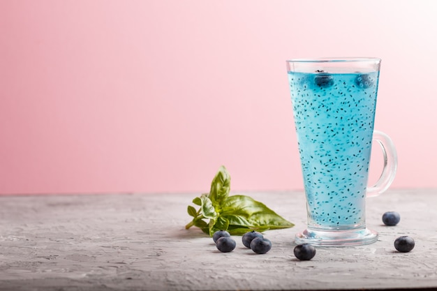 Verre de boisson aux bleuets avec des graines de basilic sur fond gris et rose