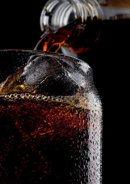 Verre de boisson gazeuse cola froide avec des glaçons sur fond noir. Macro avec des gouttes de rosée.