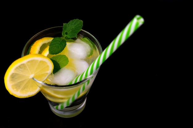 Un verre de boisson saine à base de citrons à la menthe avec des glaçons sur fond noirCopier l'espace