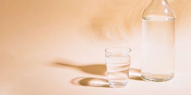 Verre et bouteille avec de l'eau sur une surface pastel