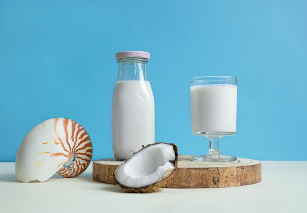 Un verre et une bouteille de lait de coco végétalien un morceau de noix de coco et un coquillage exotique