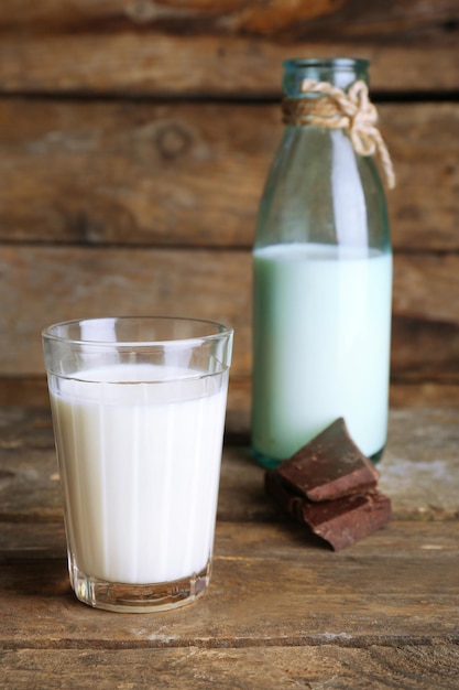 Verre et bouteille de lait avec des morceaux de chocolat sur fond de planches de bois rustiques