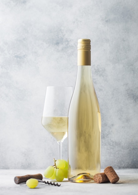 Verre et bouteille de vin blanc d'été avec raisins, bouchons et tire-bouchon sur fond de pierre clair.