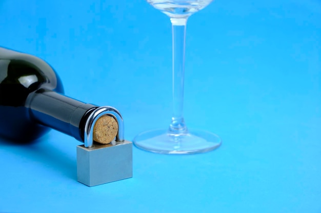 Verre et bouteille de vin avec serrure sur le cou sur fond bleuConcept interdiction d'alcool