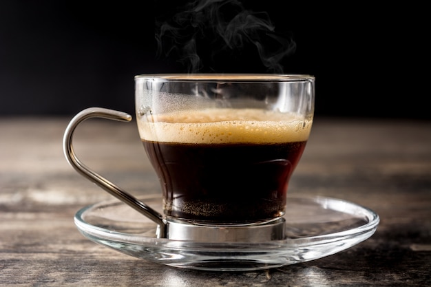 Verre à café chaud avec de la fumée sur une table en bois.