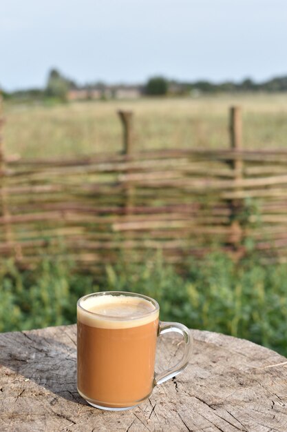 Un verre de café clair sur une terrasse en bois.