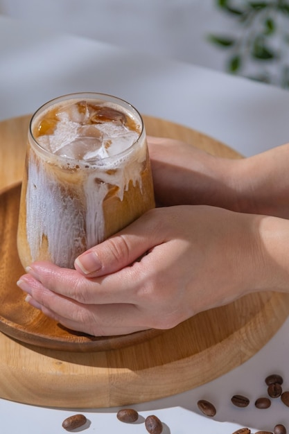 Verre d'un café glacé infusé avec du lait crémeux et servi avec des biscuits Verre de boisson au café froid avec de la glace et du lait à la crème sur une table blanche utilisée main tenant une tasse de rafraîchissement