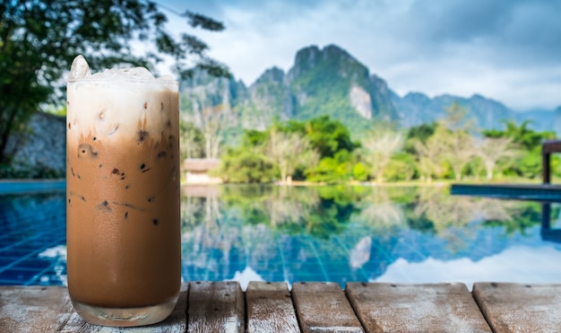 Un verre de café glacé sur la table en bois au bord de la piscine