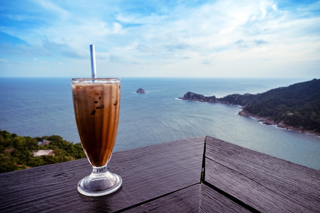 Verre à café latte glacé sur la terrasse de la table en bois avec vue sur la mer depuis le sommet de la montagne