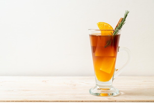 Un verre de café noir américain glacé et couche de jus d'orange et de citron décoré de romarin et de cannelle sur fond de bois