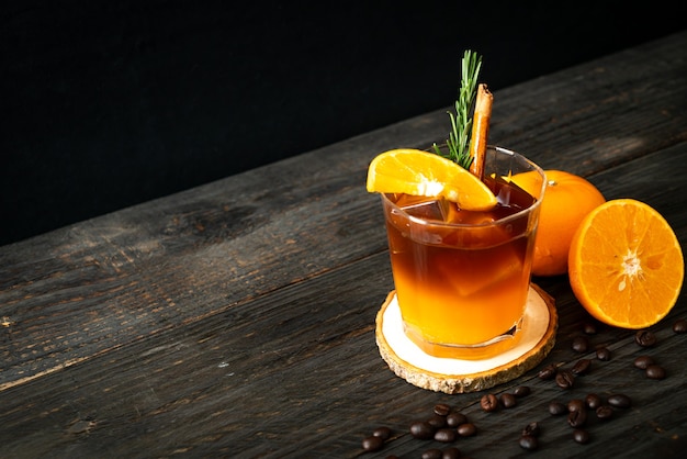 Un verre de café noir américain glacé et une couche de jus d'orange et de citron décoré de romarin et de cannelle