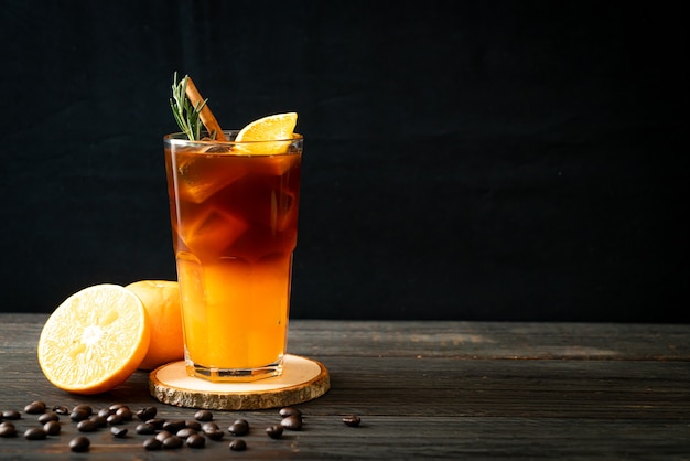 Un verre de café noir américain glacé et une couche de jus d'orange et de citron décoré de romarin et de cannelle