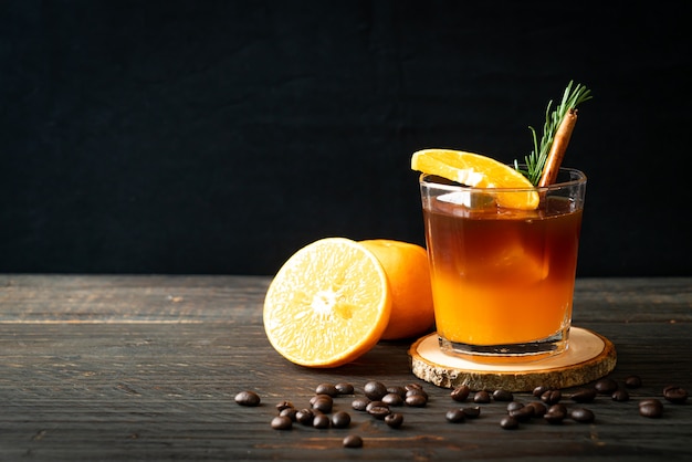 Un verre de café noir américain glacé et une couche de jus d'orange et de citron décoré de romarin et de cannelle