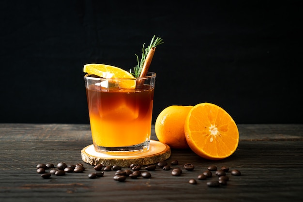 Un verre de café noir americano glacé et une couche de jus d'orange et de citron décoré de romarin et de cannelle