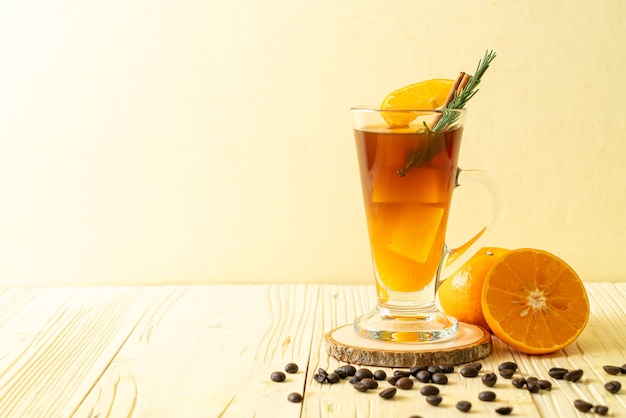 Un verre de café noir americano glacé et une couche de jus d'orange et de citron décoré de romarin et de cannelle