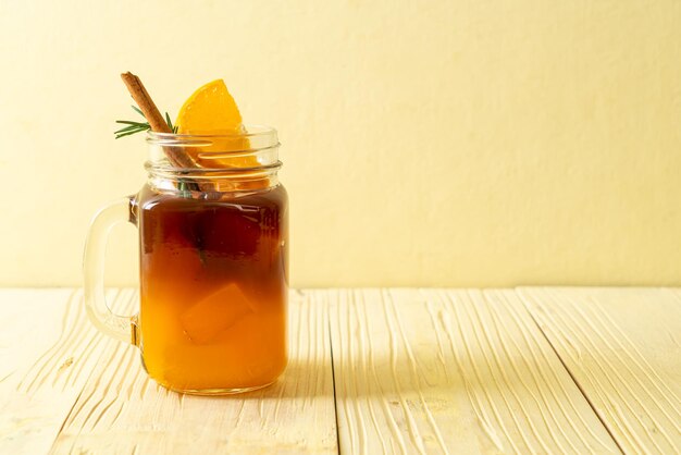 Un verre de café noir americano glacé et une couche de jus d'orange et de citron décoré de romarin et de cannelle