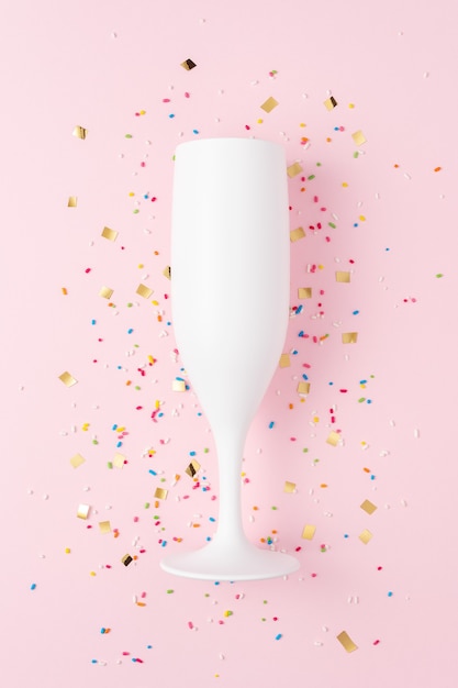 Verre à champagne blanc avec des confettis sur fond rose.
