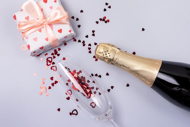 Verre à champagne avec boîte-cadeau de confettis coeurs rouges Bouteille de champagne sur papier bleu