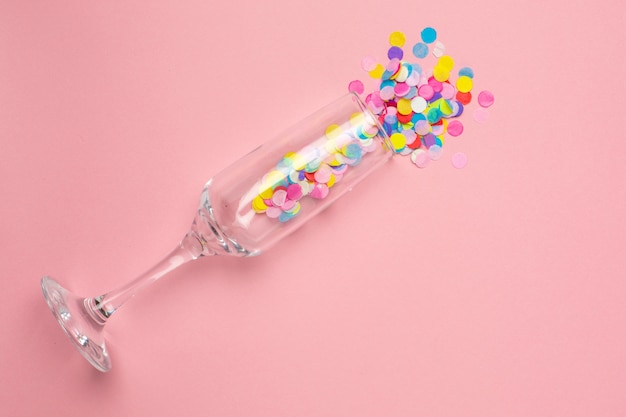 Verre de champagne avec des confettis multicolores sur rose