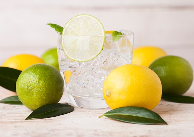 Verre de citron et de citron vert frais encore de l'eau d'été avec des citrons crus sur bois. Vue de dessus